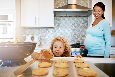 Buy stock photo Cropped shot of a little boy reaching out for a freshly baked cookie with his mother watching in the background