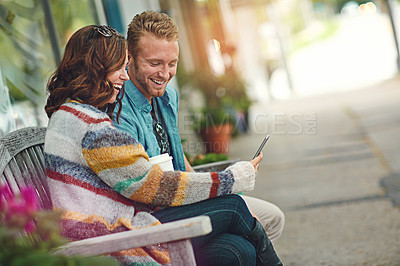 Buy stock photo Shot of a happy young couple using a smartphone together while spending the day downtown