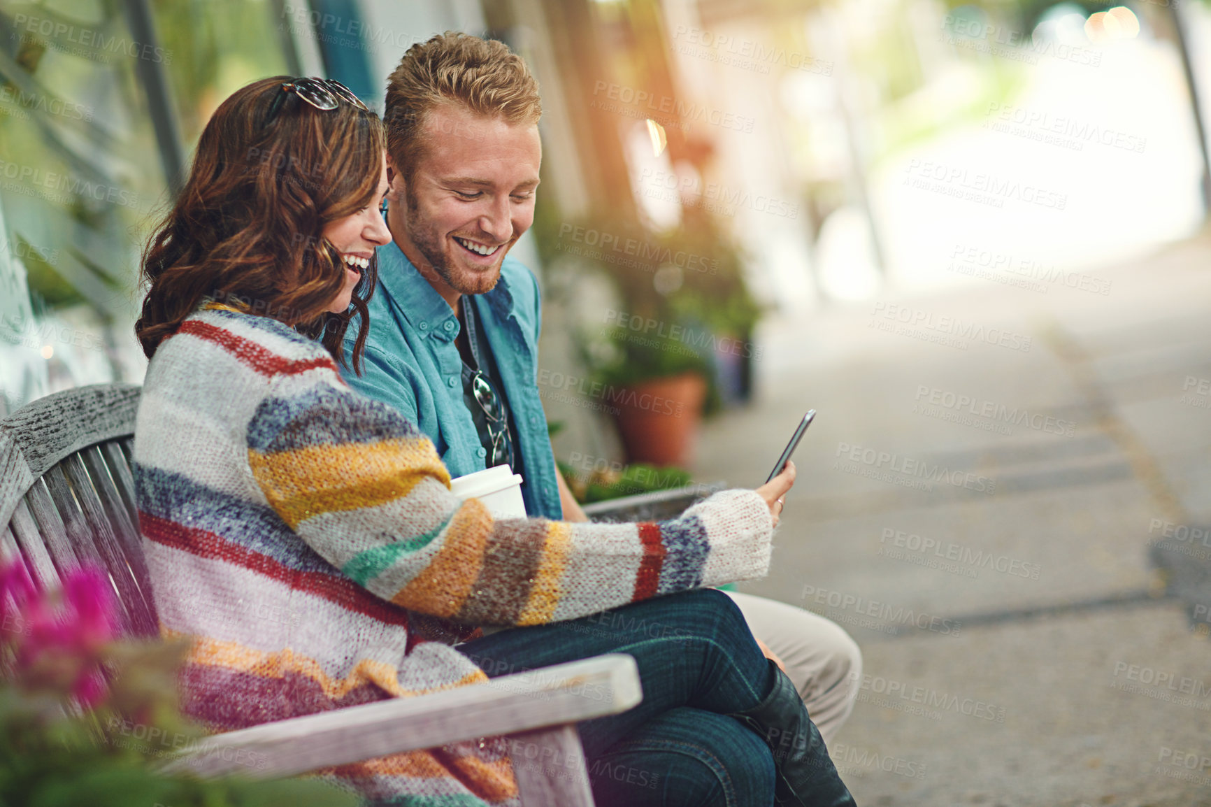 Buy stock photo Shot of a happy young couple using a smartphone together while spending the day downtown