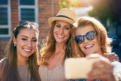 Buy stock photo Cropped shot of three young girlfriends taking selfies while outdoors