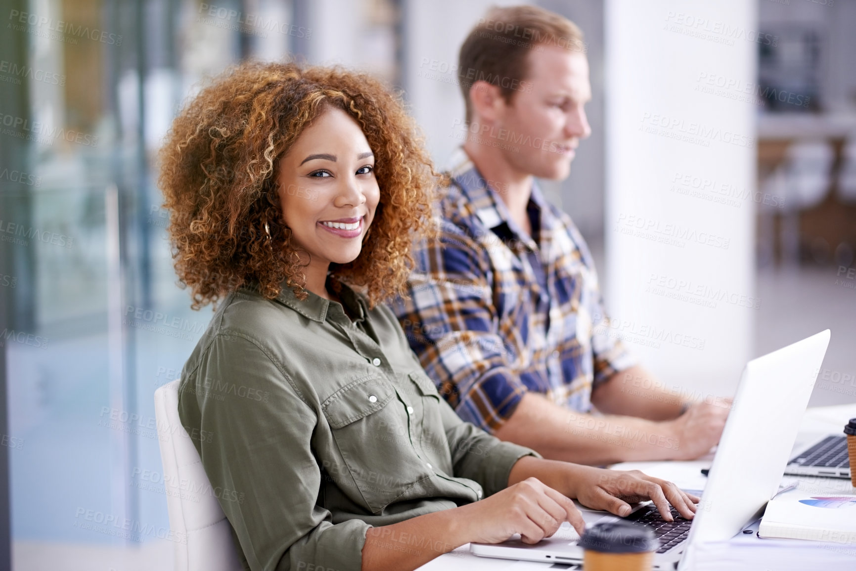 Buy stock photo Portrait of a young designer working on a laptop with her colleague in the background