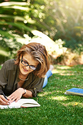 Buy stock photo Shot of an attractive young woman writing in her diary while outside on the grass
