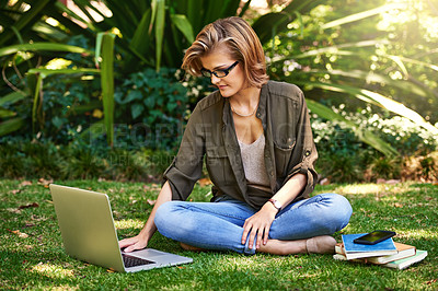 Buy stock photo Shot of an attractive young woman using her laptop while outside on the grass