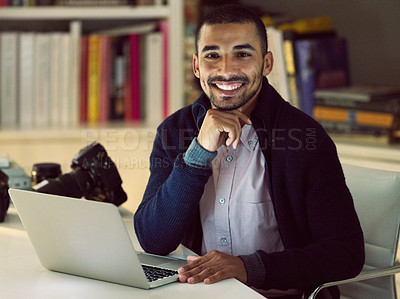 Buy stock photo Portrait of a smiling young photographer working on a laptop in his home office in the early evening