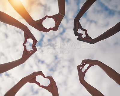 Buy stock photo Low angle shot of a group of unidentifiable people making heart shapes with their hands against a cloudy sky