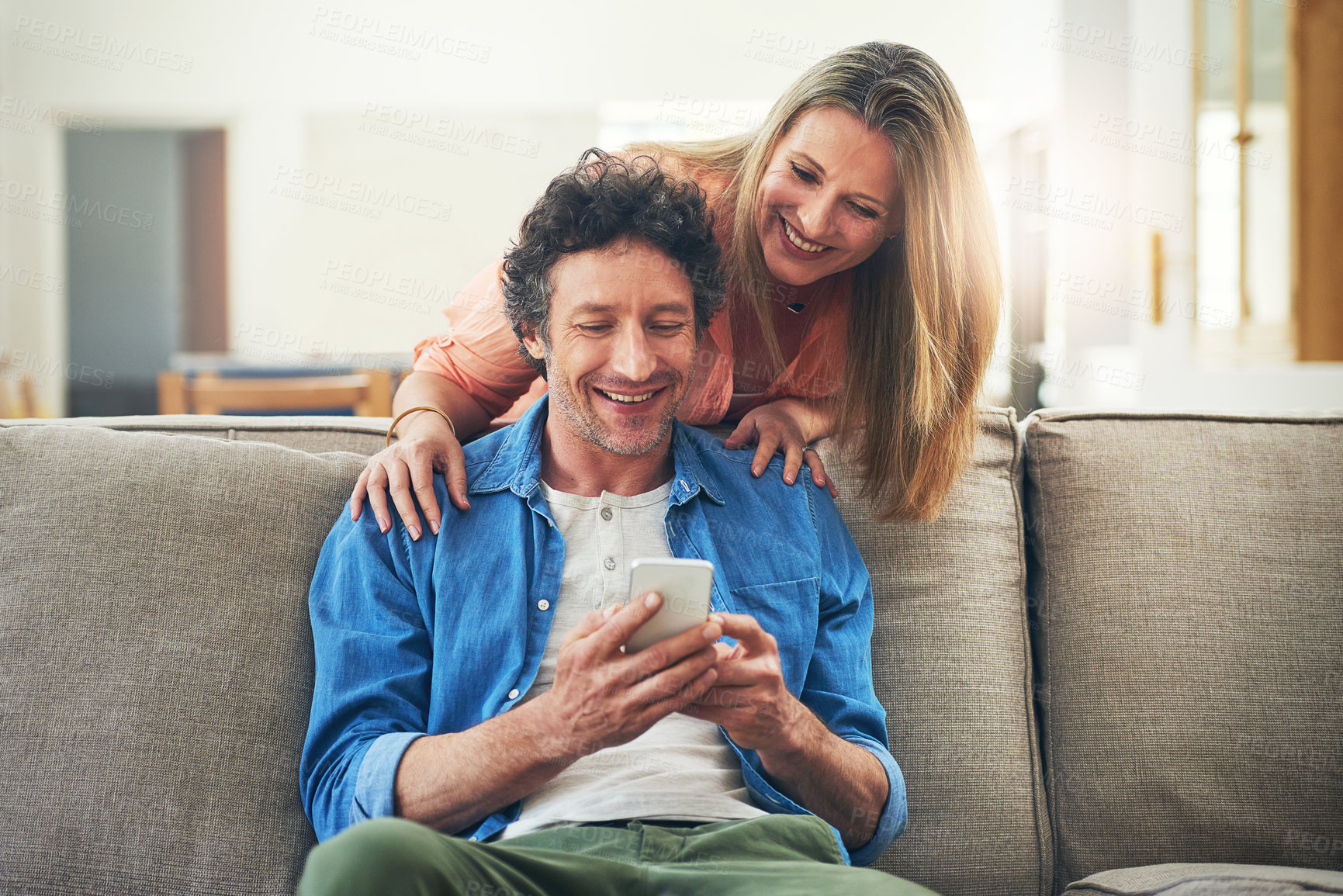Buy stock photo Mature, couple and happy on couch with phone for reading online news, social media scroll and embrace in home. People, hug and laughing with smartphone for funny meme, bingo or digital gaming on sofa