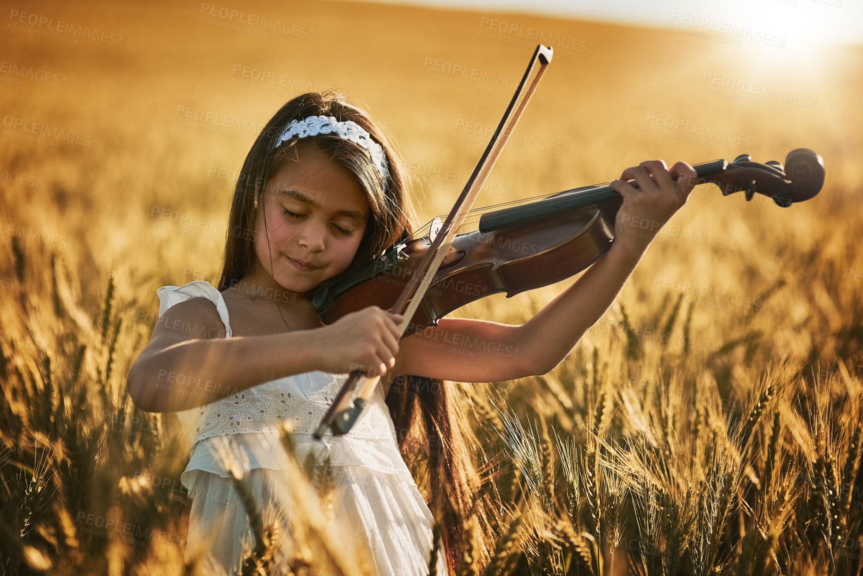 Buy stock photo Shot of a cute little girl playing the violin while standing in a cornfield