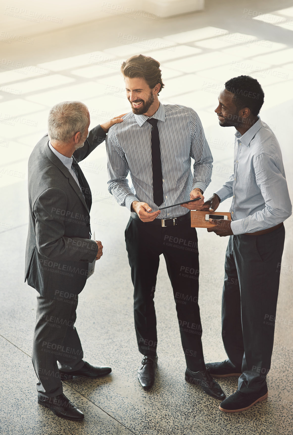 Buy stock photo High angle shot of a group of businessmen talking together while standing in an office lobby