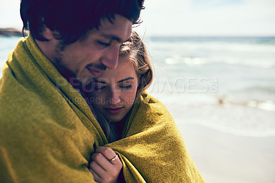 Buy stock photo Cropped shot of an affectionate young couple wrapped in a blanket on the beach