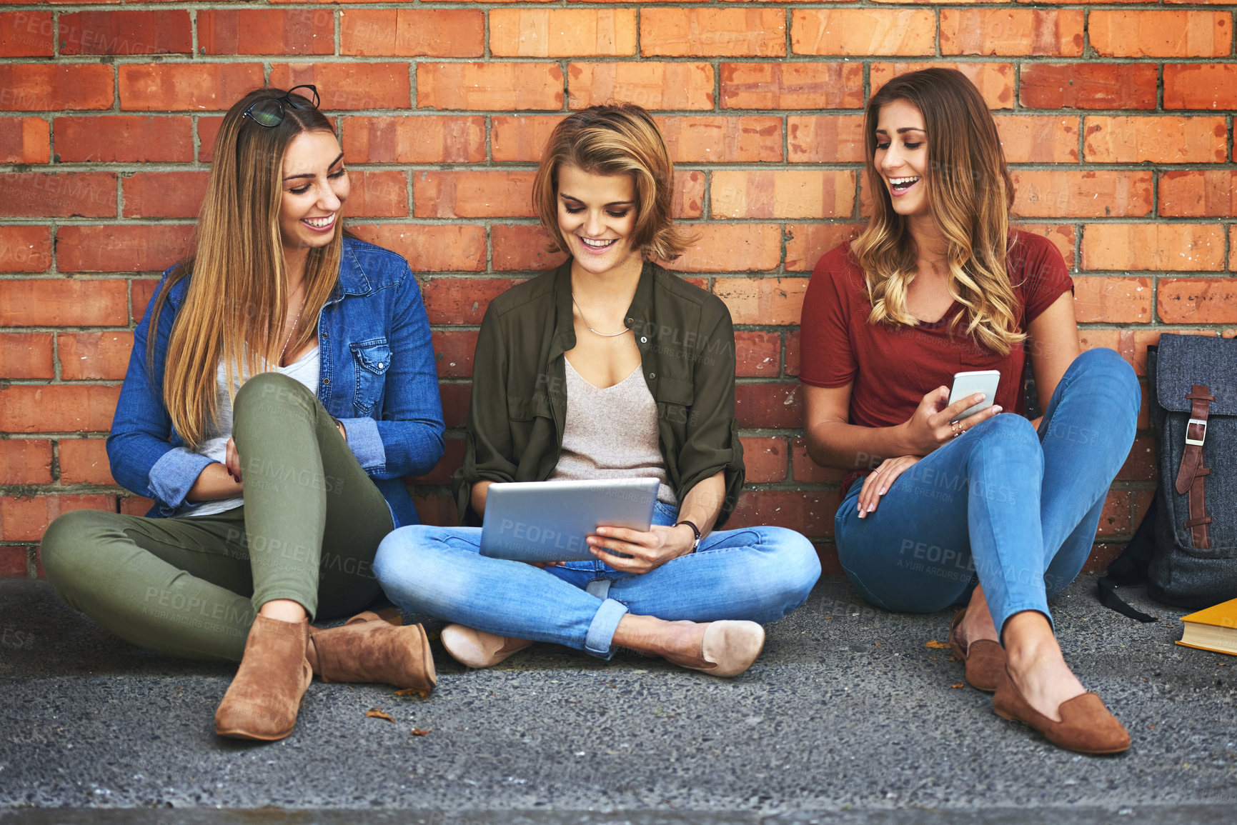 Buy stock photo Shot of three smiling female university students sitting together outside on campus using a digital tablet