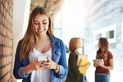 Buy stock photo Shot of a smiling female university student standing on campus using a cellphone with friends in the background