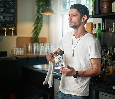 Buy stock photo Shot of a young waiter daydreaming while polishing a glass behind the bar