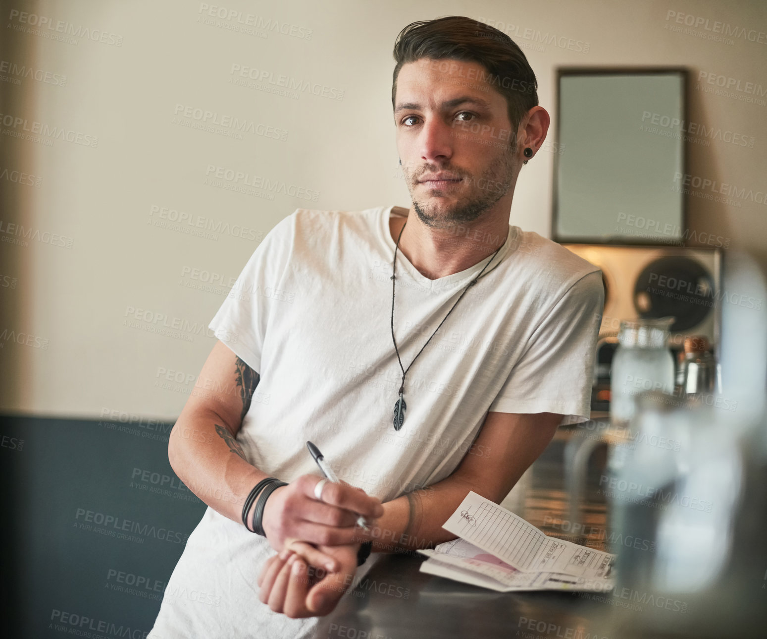 Buy stock photo Portrait of a serious young bartender leaning on the bar counter