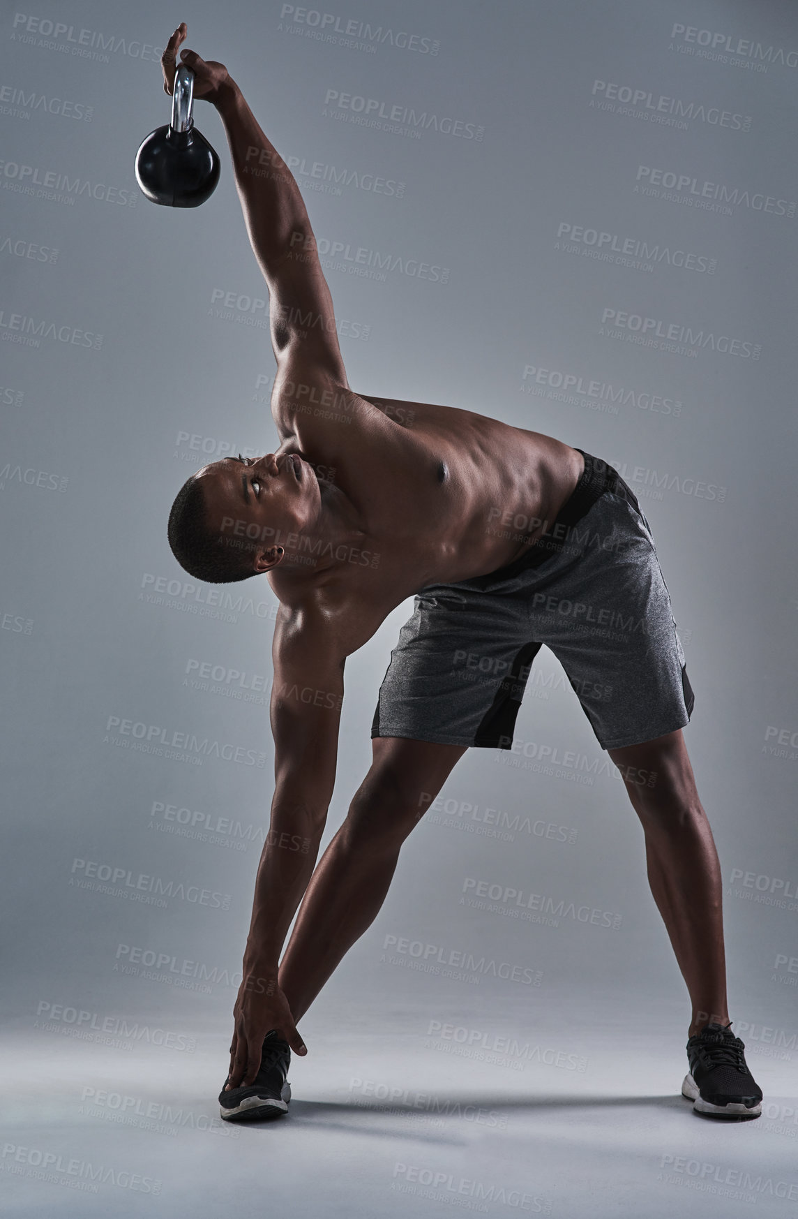 Buy stock photo Full length shot of an athletic young man working out with a kettle bell