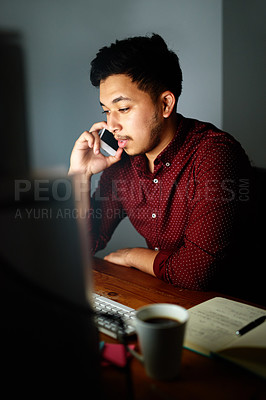 Buy stock photo Shot of a young male designer talking on the phone and working on his computer late at night