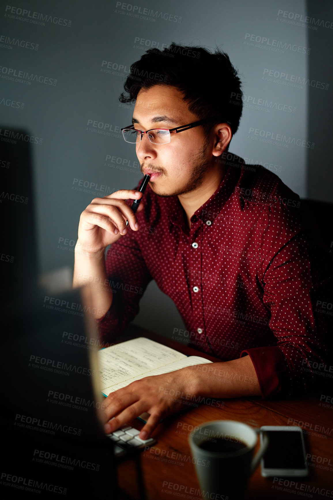 Buy stock photo Shot of a young male designer working on his computer late at night