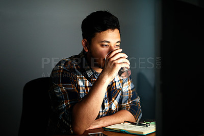 Buy stock photo Shot of a young male designer drinking water while working on his computer late at night