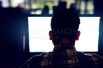 Buy stock photo Rearview shot of a young male designer working on his computer late at night