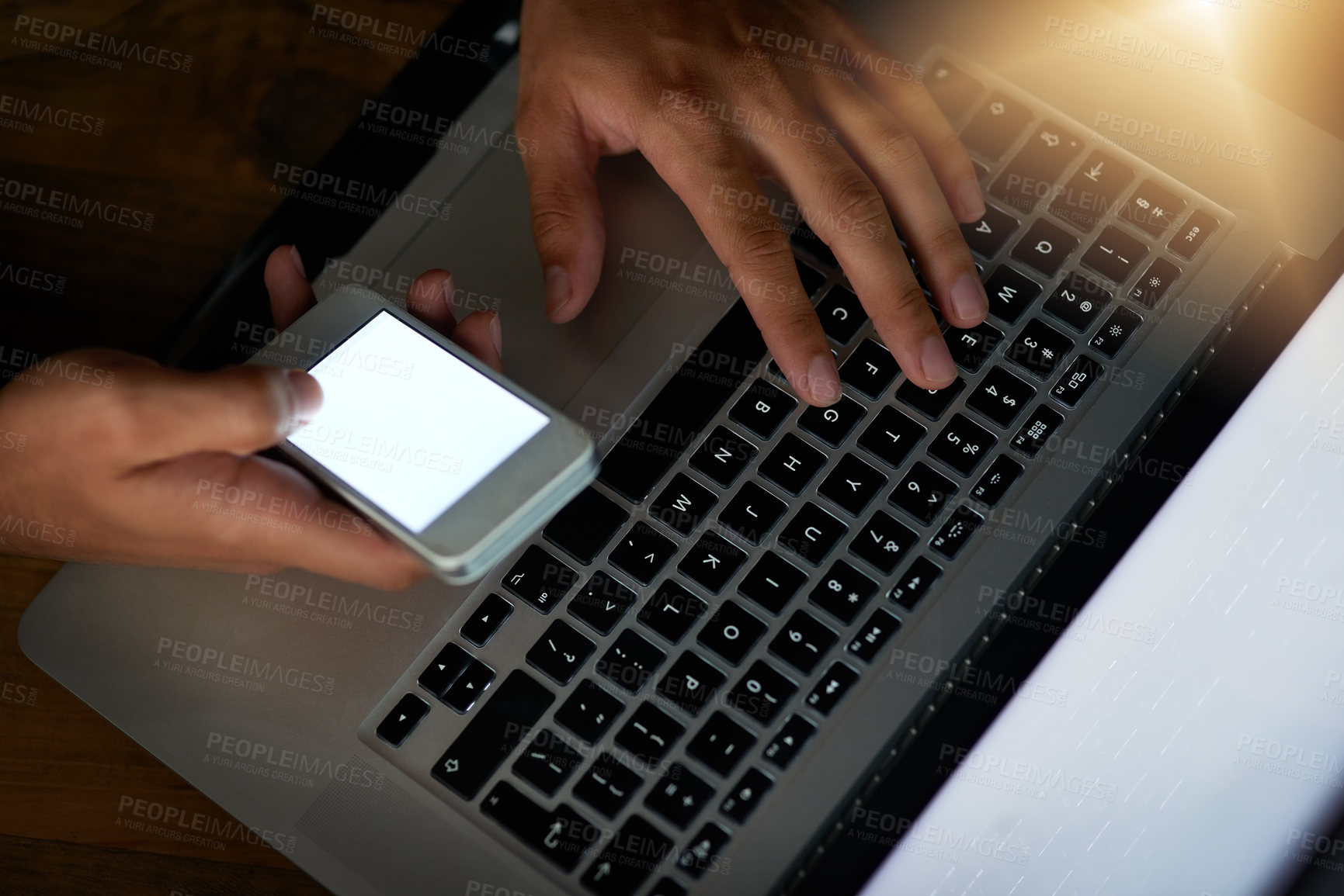 Buy stock photo High angle shot of a hacker using a cellphone to cracking a computer code in the dark