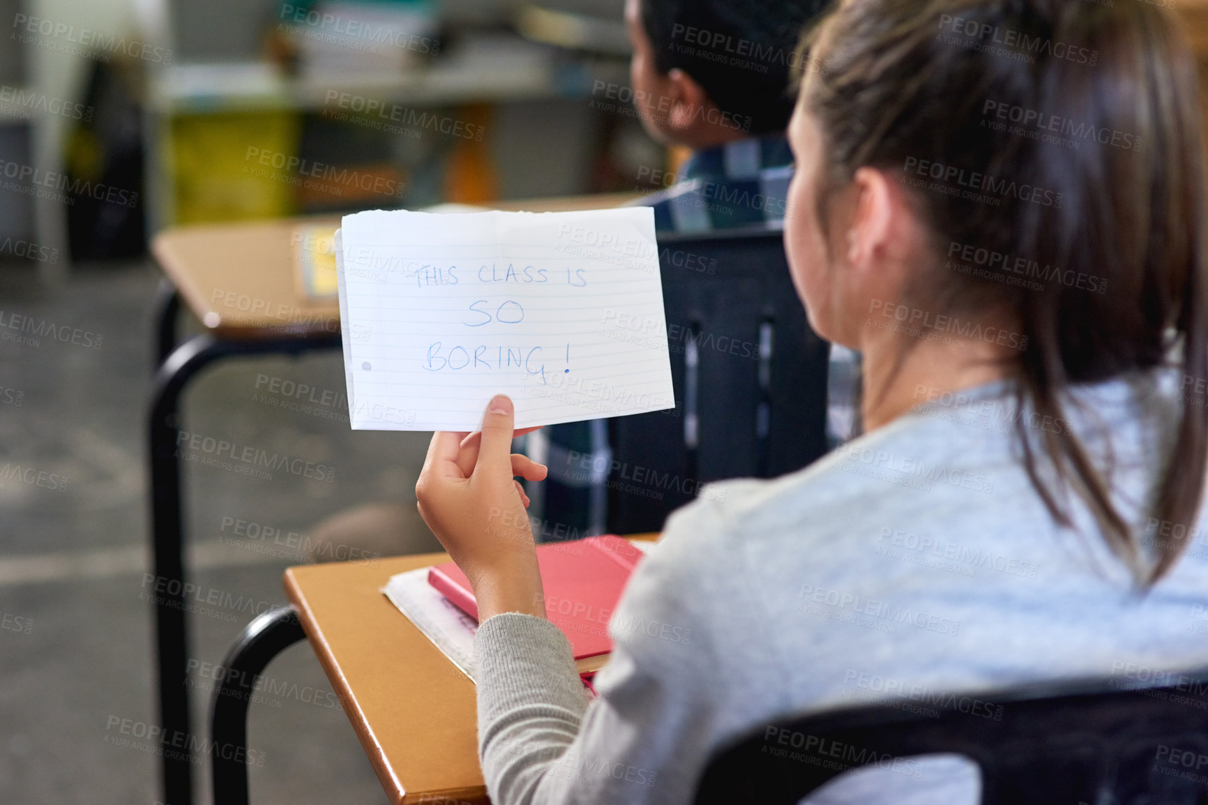 Buy stock photo Rearview shot of an unidentifiable schoolgirl reading a note in class