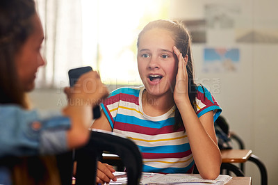 Buy stock photo Shot of a young schoolgirl looking at her classmate's smartphone in awe in class