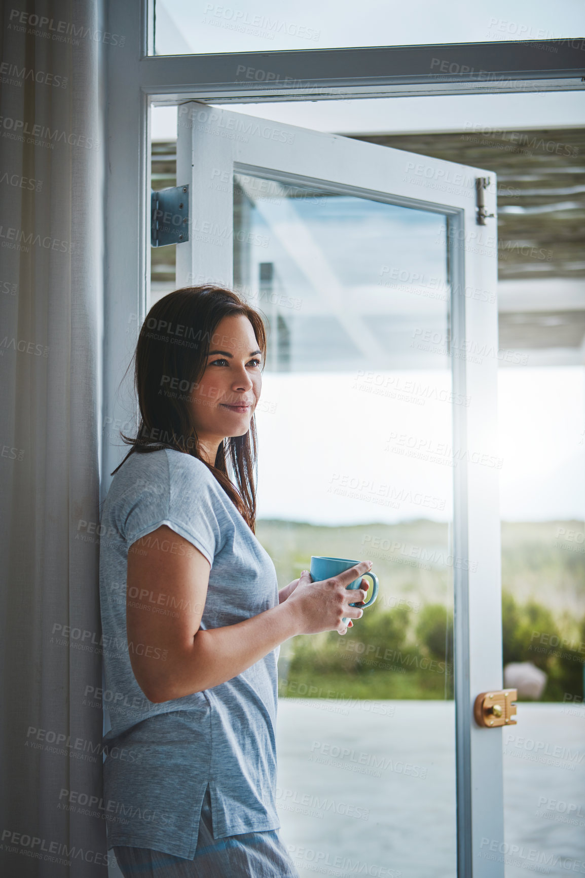 Buy stock photo Cropped shot of an attractive young woman enjoying a coffee by her patio door