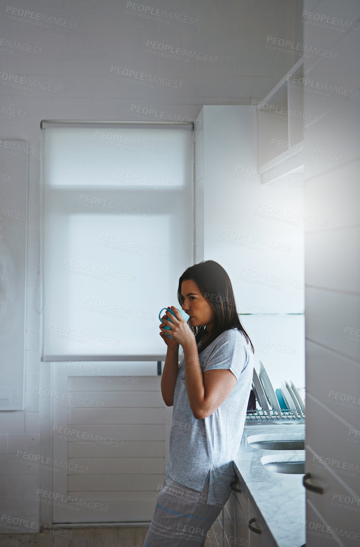 Buy stock photo Cropped shot of an attractive young woman enjoying a coffee while standing in the kitchen