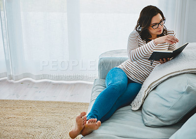 Buy stock photo Shot of a young woman relaxing on the sofa and reading a book at home
