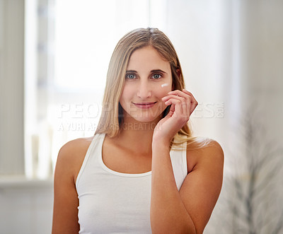 Buy stock photo Portrait of a beautiful young woman applying moisturizer to her face in the bathroom at home