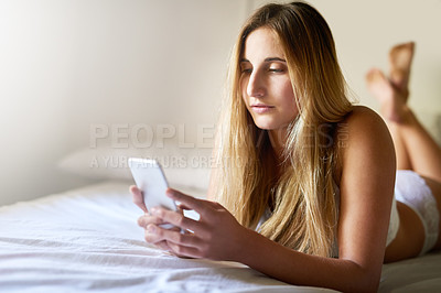 Buy stock photo Shot of a beautiful young woman using her smartphone while relaxing on her bed