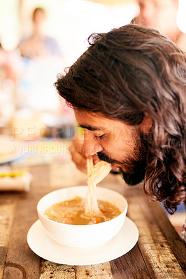 Buy stock photo Shot of a young man eating a bowl of noodles in a restaurant in Thailand