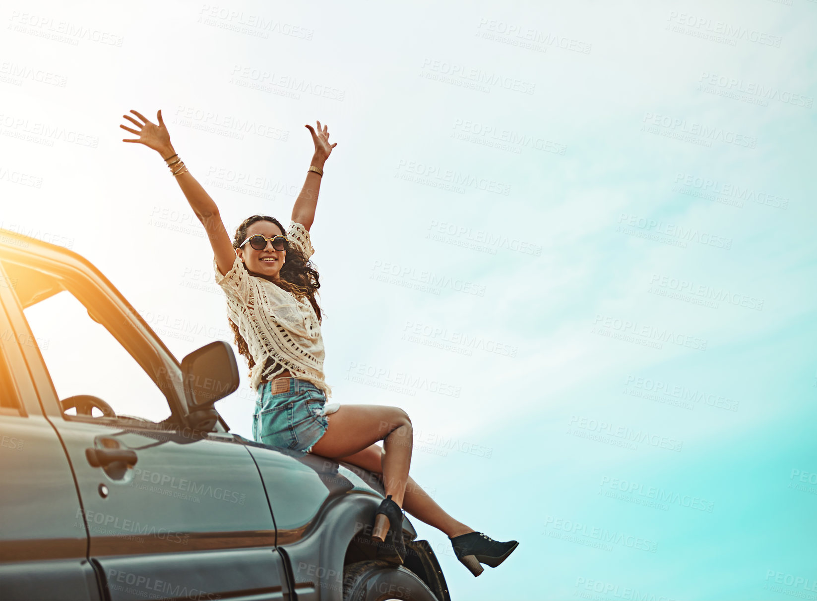 Buy stock photo Portrait of a young woman sitting on a car with her arms outstretched while on a roadtrip