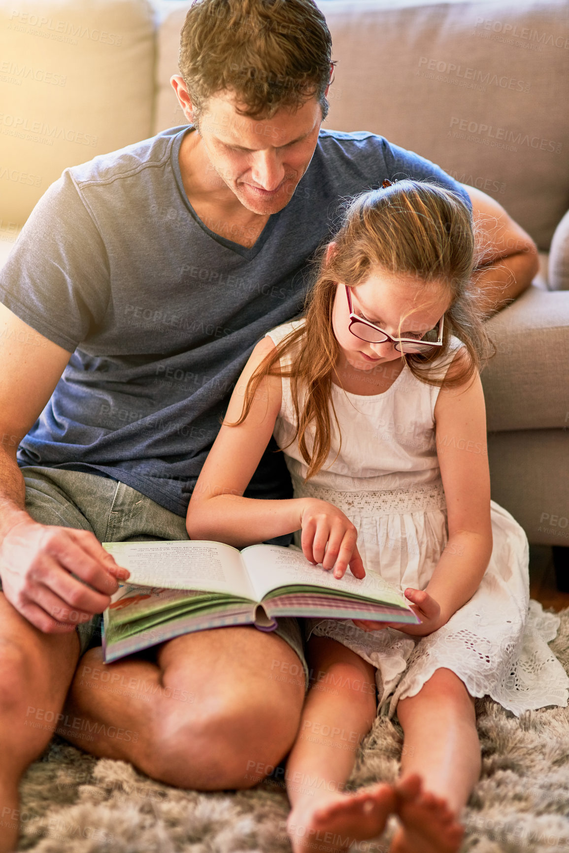 Buy stock photo Cropped shot of a father and his little daughter reading a book together at home