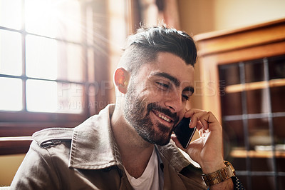 Buy stock photo Shot of a handsome young man smiling and talking on a cellphone at home