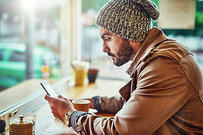 Buy stock photo Shot of a stylish young man reading a text message while sitting at a counter in a cafe