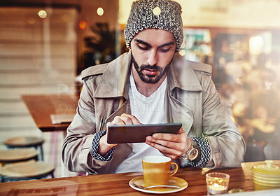 Buy stock photo hot of handsome young man using a digital tablet while sitting at a counter in a cafe