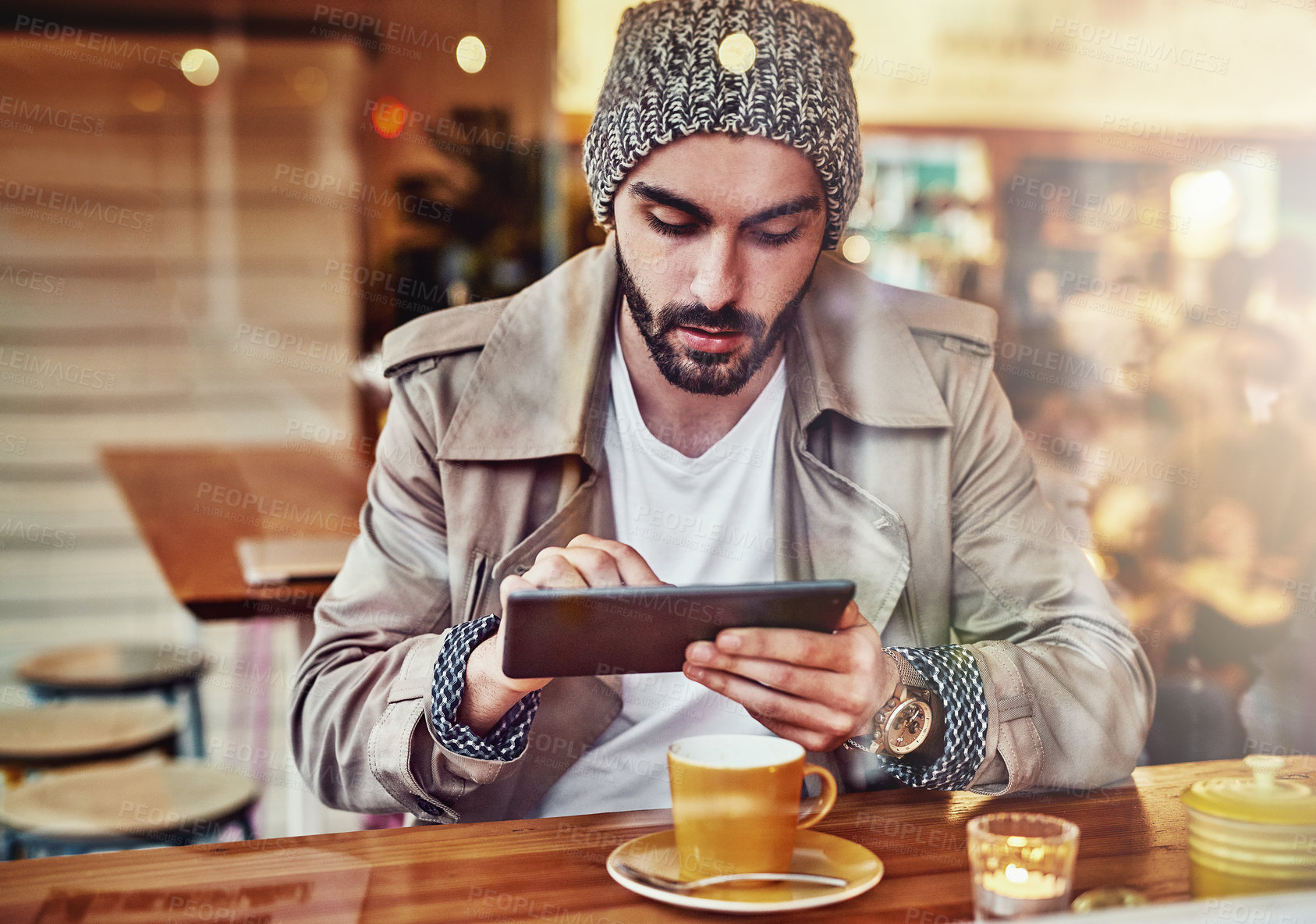 Buy stock photo hot of handsome young man using a digital tablet while sitting at a counter in a cafe