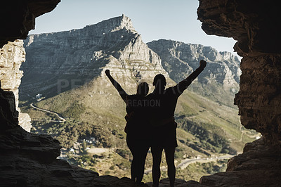 Buy stock photo Rearview shot of young couple standing on a mountain cliff with their arms raised