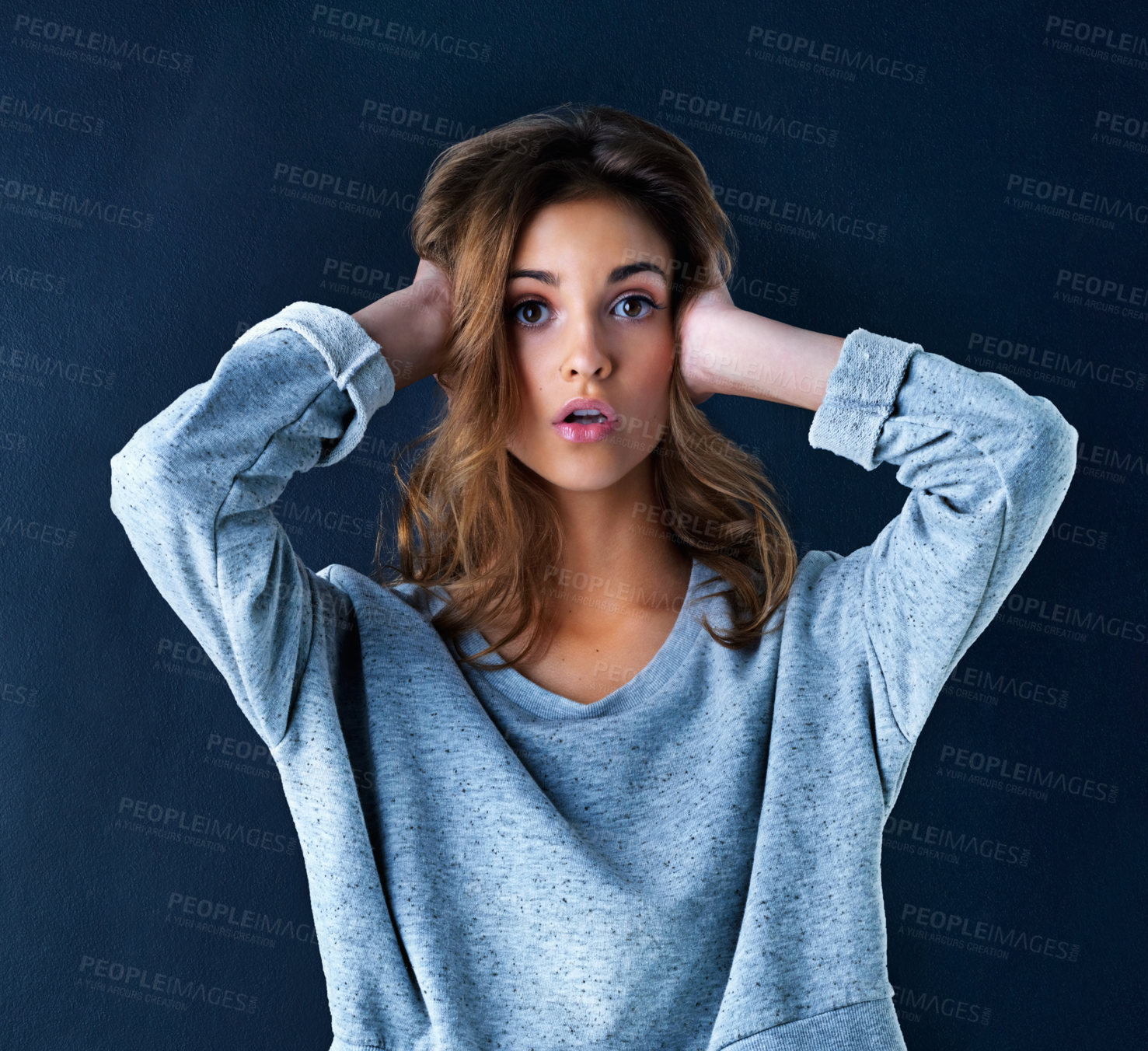 Buy stock photo Studio portrait of a cute teenage girl looking surprised with her hands over her ears posing against a dark background