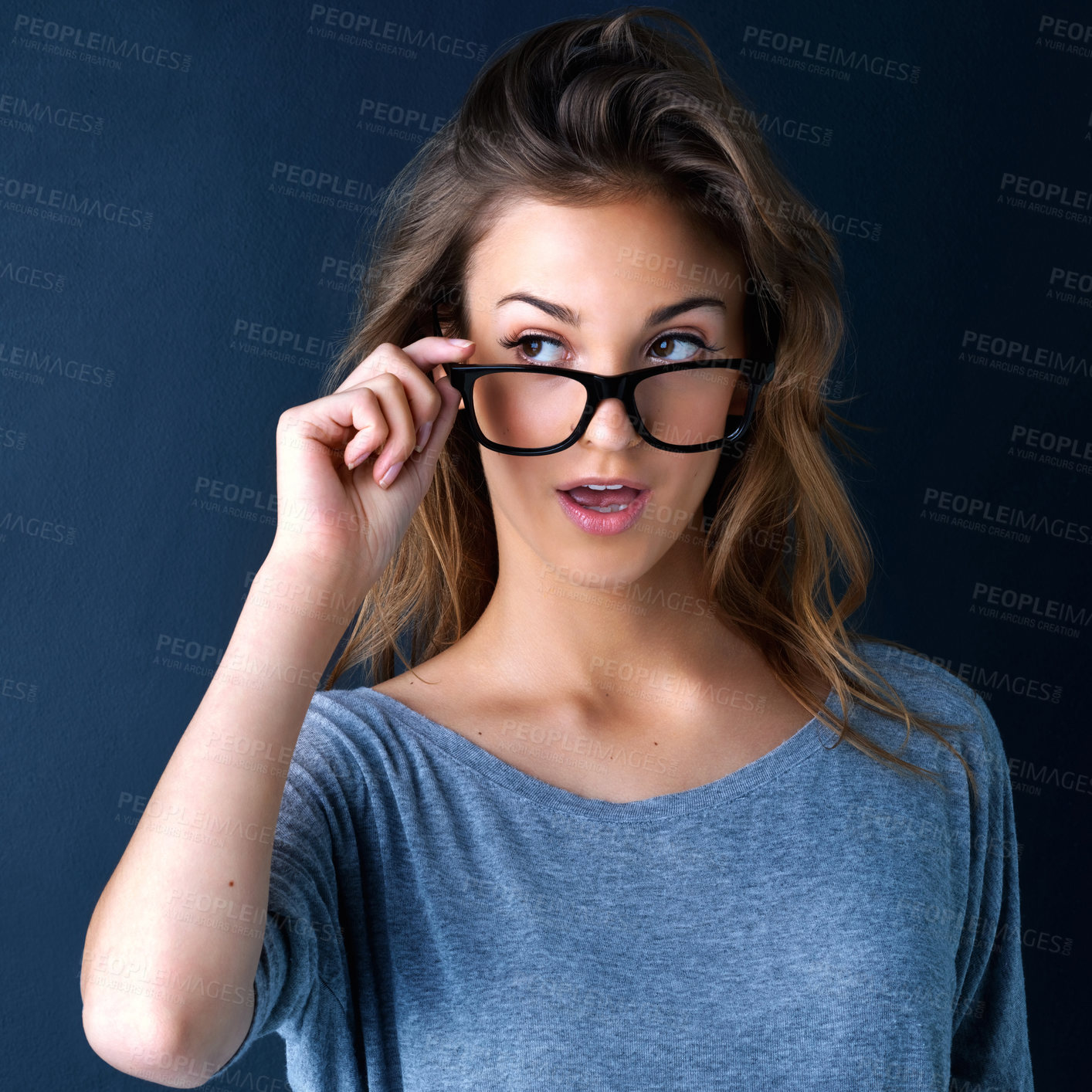 Buy stock photo Studio shot of a cute teenage girl in glasses raising her eyebrows in surprise posing against a dark background