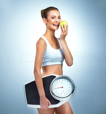 Buy stock photo Portrait of a health-conscious young woman posing with an apple and a scale in studio