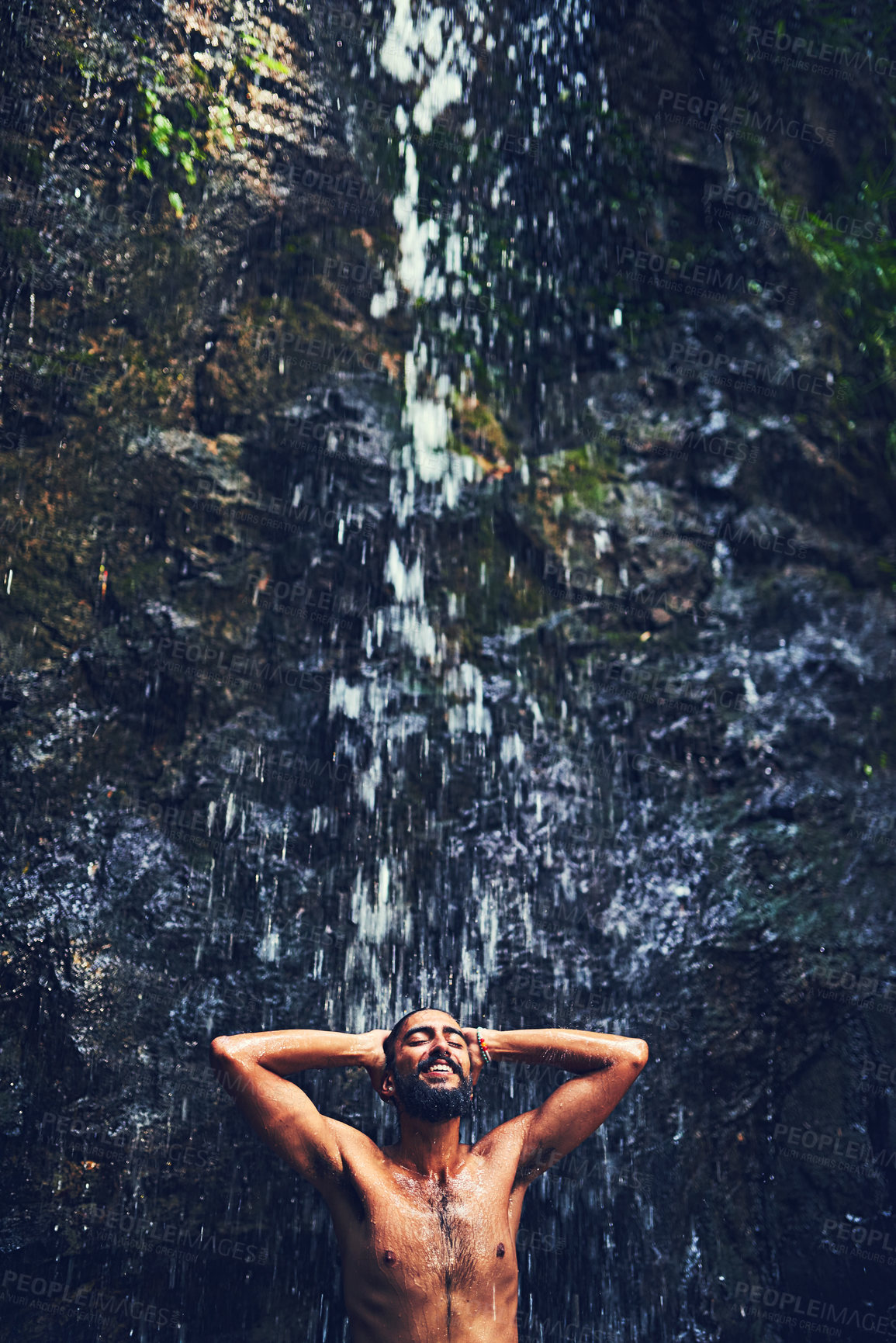 Buy stock photo Shot of a happy young tourist standing under a waterfall in the jungle