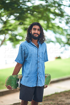 Buy stock photo Portrait of a smiling young man carrying a skateboard standing outside on a sunny day