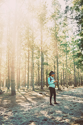 Buy stock photo Full length shot of an athletic young woman sending a text while jogging in the woods