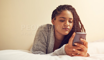 Buy stock photo Shot of a young woman lying on bed with her cellphone