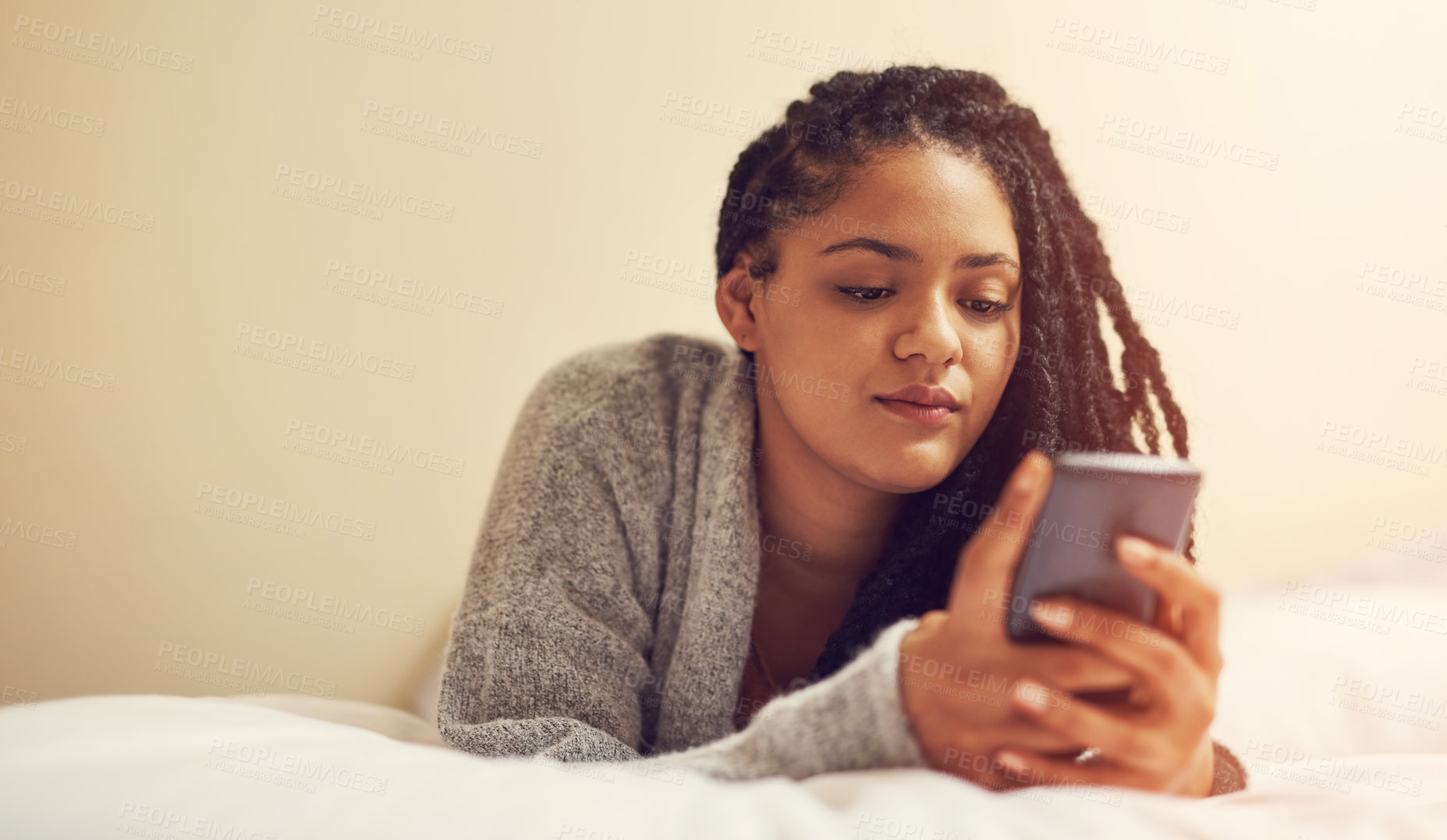 Buy stock photo Shot of a young woman lying on bed with her cellphone