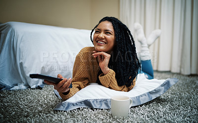 Buy stock photo Shot of a young woman lying on the floor with a remote control