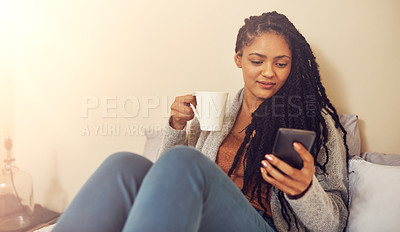 Buy stock photo Shot of a young woman drinking coffee and using her cellphone
