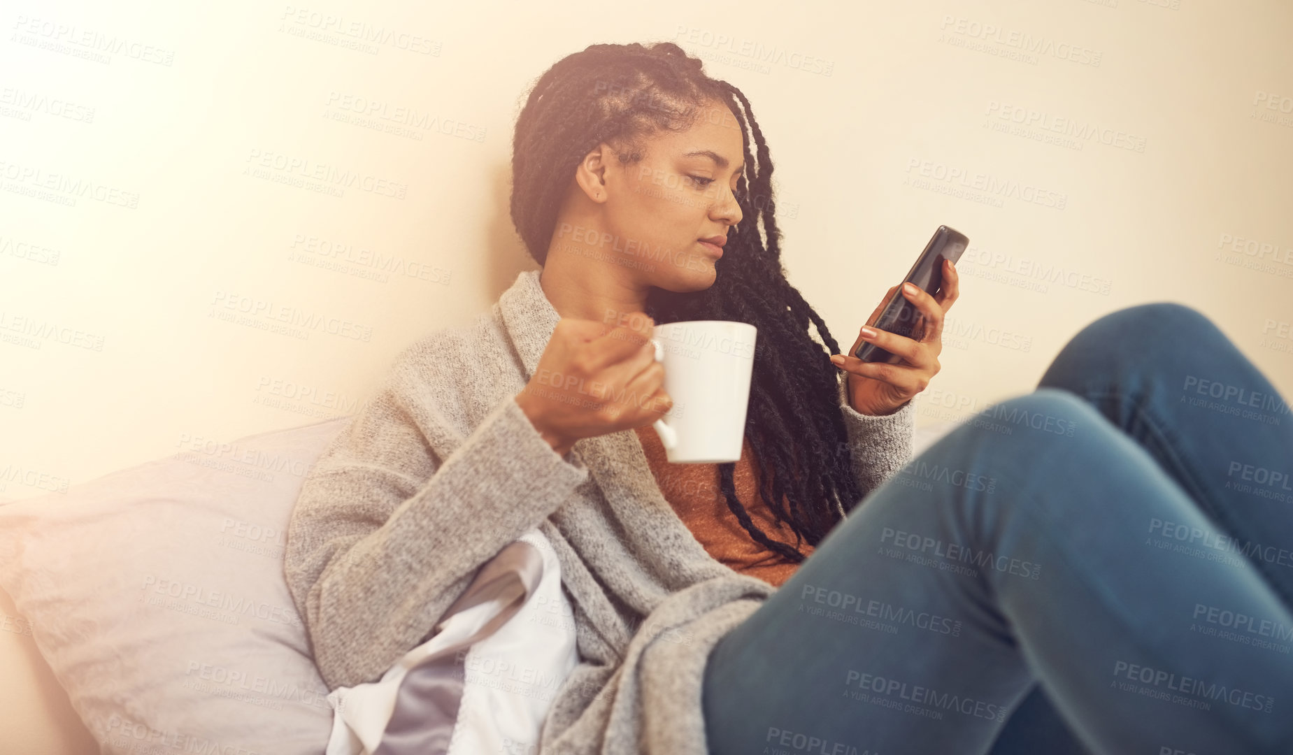 Buy stock photo Shot of a young woman drinking coffee and using her cellphone