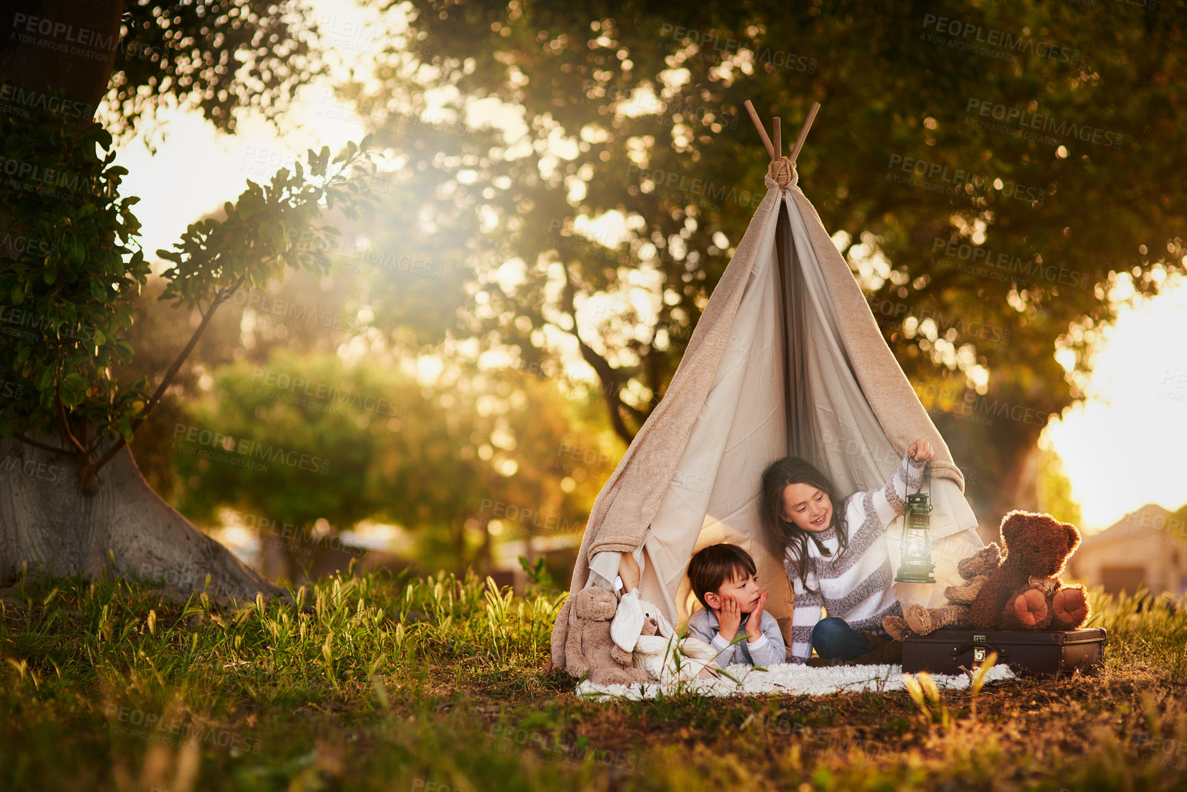 Buy stock photo Teepee, kids and playing in garden tent outdoor in nature for camping, fun and adventure with imagination. Cloth, light and fantasy house for children in forest with blanket, suitcase and teddy bear